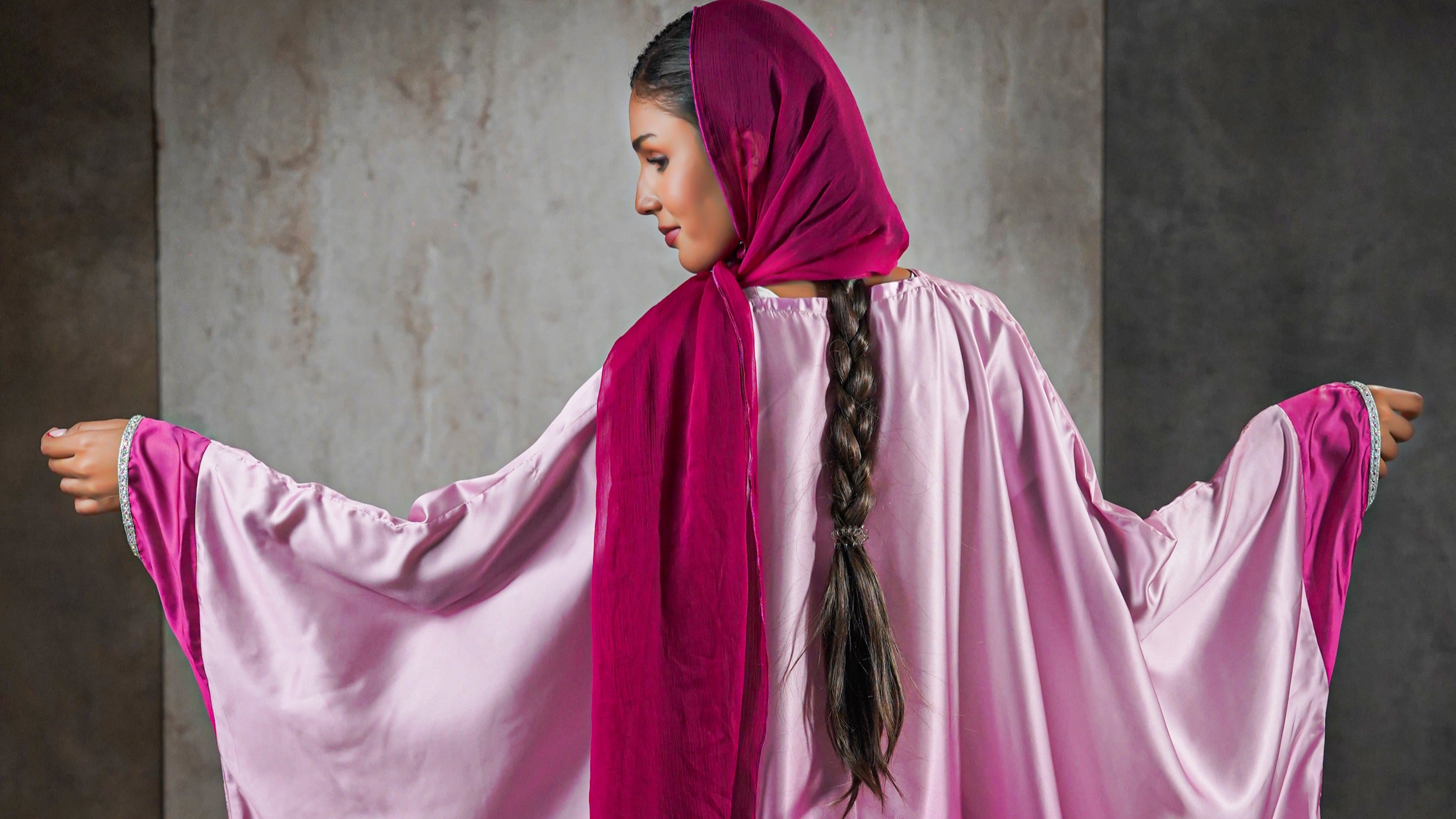 Woman wearing a pink outfit with a magenta hijab against a gray background